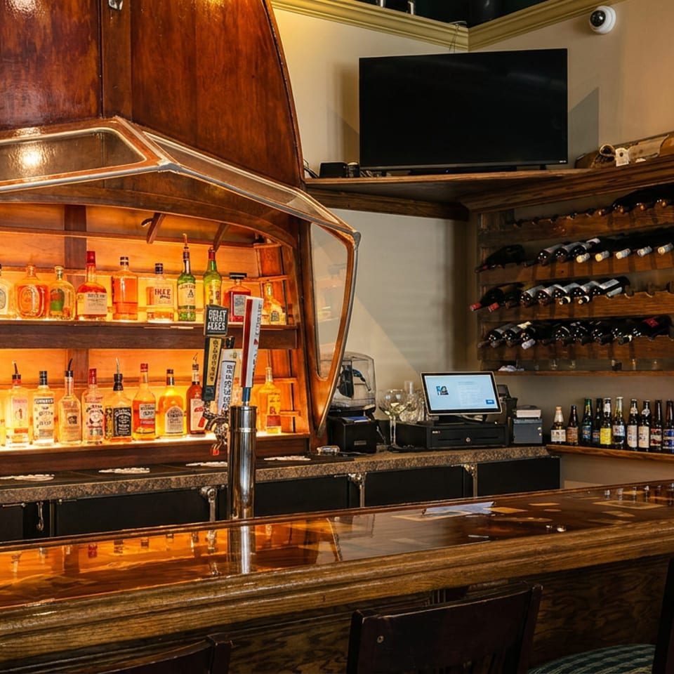 Warmly lit restaurant bar featuring illuminated liquor shelves, rows of wine bottles, beer taps, wooden counter, and seating.