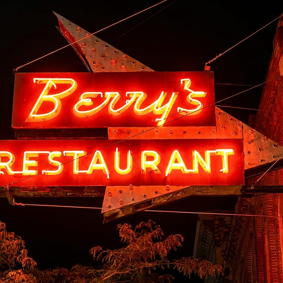 Glowing red neon sign reading “Bery’s Restaurant” mounted on a brick building at night.