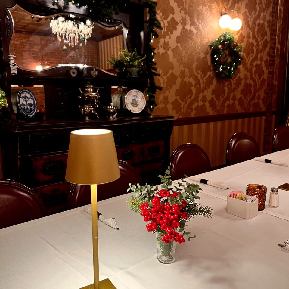 Elegant restaurant dining room with white tablecloths, candlelight, red berry centerpiece, ornate mirror, and festive Christmas garlands.